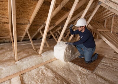 Austin Company | installing white fiberglass insulation in attic of residential home