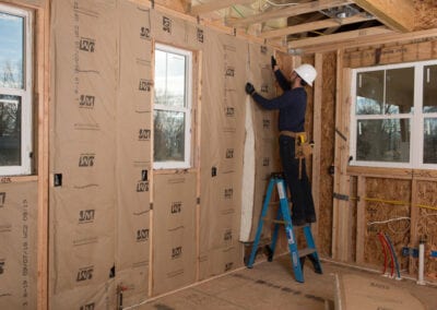 Austin Company | worker installing white fiberglass in walls of home addition